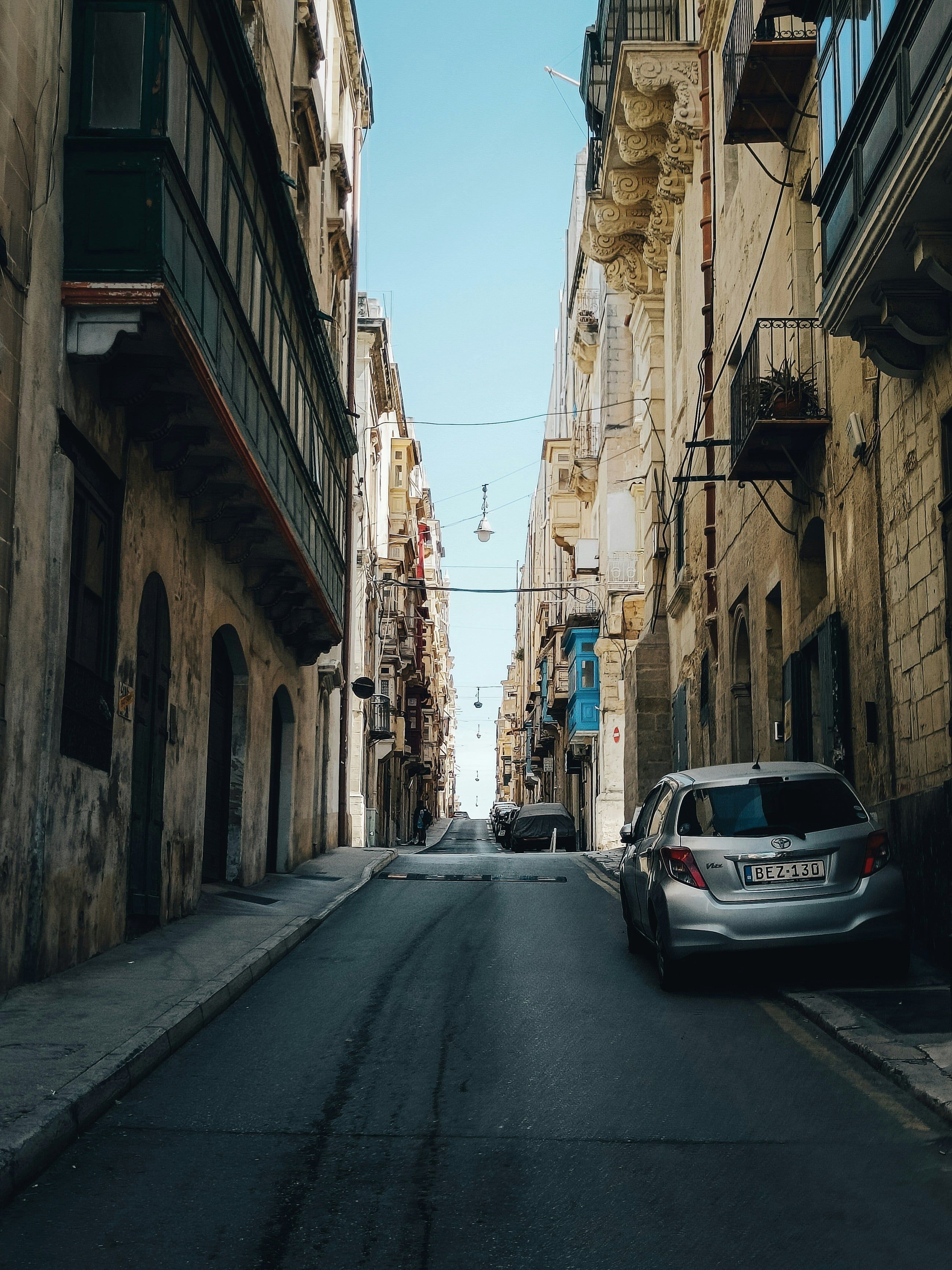 A parked car on a Valletta street between limestone buildings