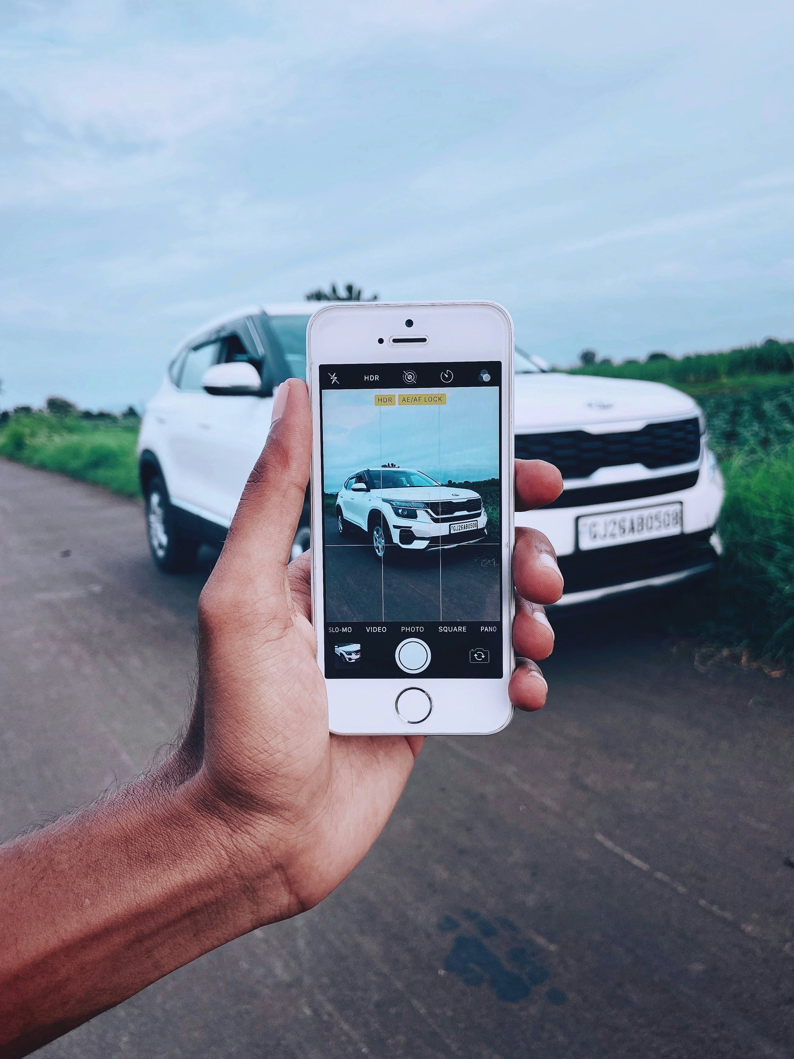 A hand holding a phone up to photograph a white car by the roadside